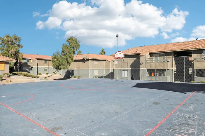 Charming apartment complex with basketball court, perfect for outdoor fun under a clear blue sky.