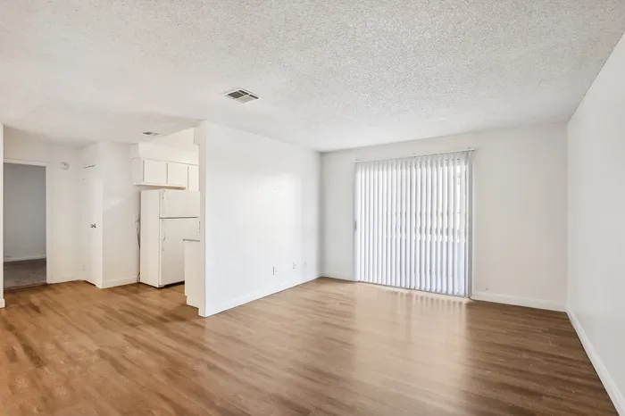 Bright, open-plan apartment interior with sleek hardwood flooring and natural light filtering through vertical blinds.