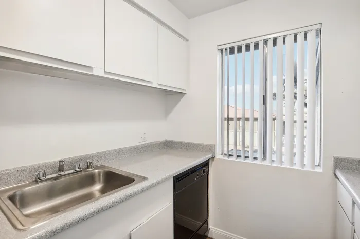 Bright, modern kitchen with sleek countertops, stainless steel sink, and large window with vertical blinds.