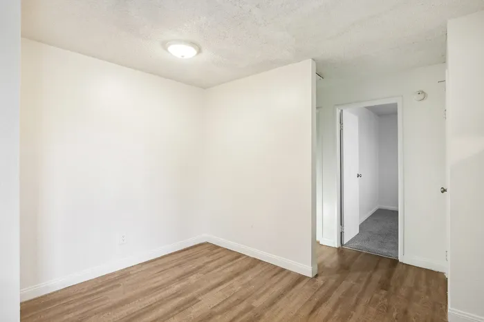 Bright room featuring fresh white walls, elegant wood flooring, and a cozy carpeted area leading to an adjacent space, ideal for creative interior design possibilities.