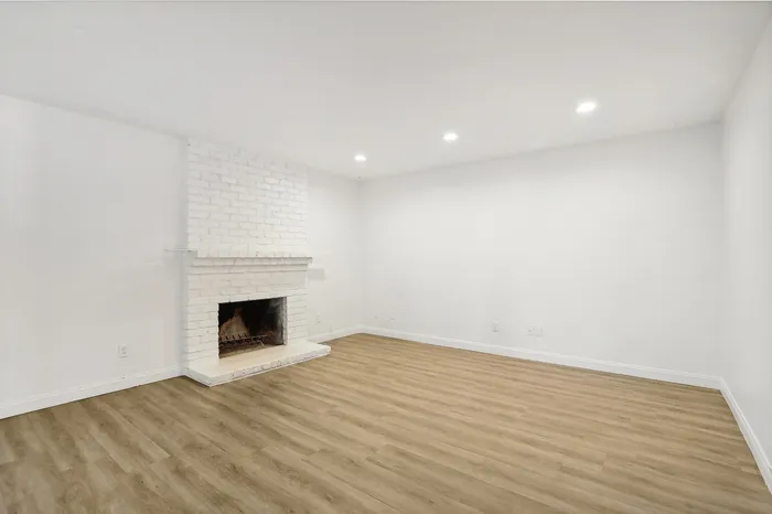Elegant living room with a white brick fireplace, sleek wood flooring, and bright recessed lighting creating a warm and inviting atmosphere.