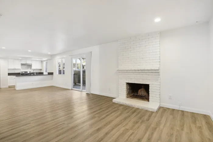Bright and airy open-concept living space with a cozy white brick fireplace, elegant hardwood floors, and modern kitchen with sleek finishes.