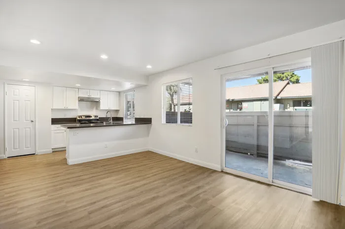 Bright open-concept living space with sleek kitchen, large windows, and sliding glass doors leading to a private patio.