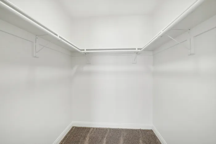 Spacious walk-in closet with ample shelving and hanging space, featuring plush carpet and bright white walls for a sleek, modern look.