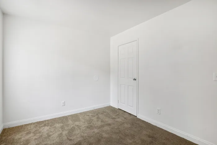 Bright and spacious empty room with soft carpet flooring and a pristine white door, ready to be transformed into your ideal space.