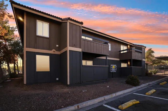 Charming two-story apartment building with wooden exterior, featuring cozy balconies against a vibrant sunset sky.