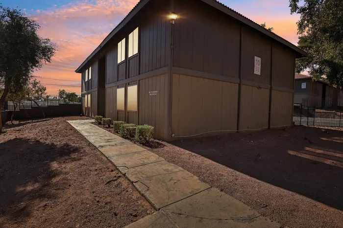 Charming apartment complex exterior with a sunset backdrop, featuring a shaded pathway lined with greenery.