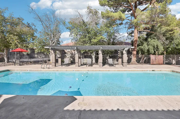 Inviting outdoor pool area with shaded pergola, surrounded by lush trees and comfortable lounge chairs, perfect for relaxation.