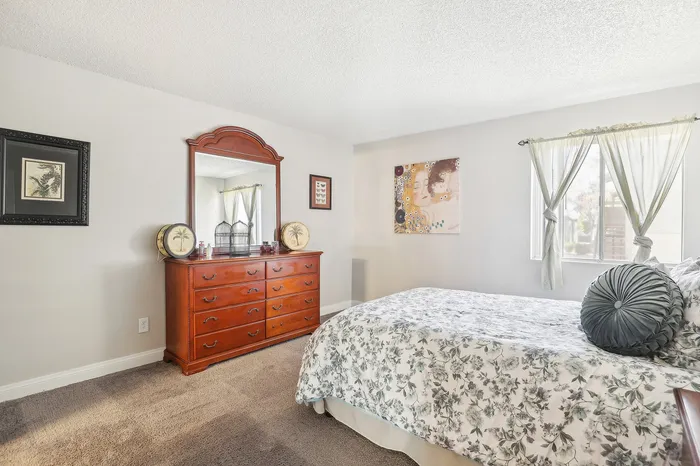 Inviting bedroom with plush floral bedding, elegant wooden dresser with mirror, and bright natural light streaming through the window.