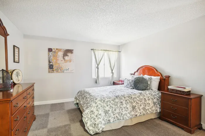 Inviting bedroom featuring a plush floral bed, elegant wooden furniture, and soft natural light streaming in.
