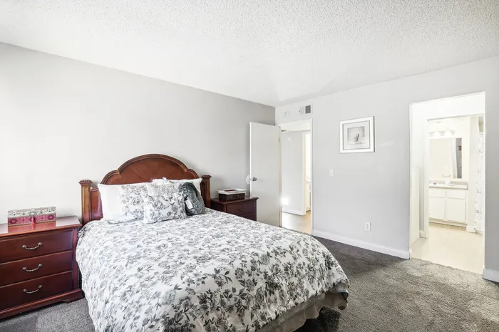 Inviting bedroom with elegant wooden furniture, chic floral bedding, and soft carpet flooring leading to a bright en-suite bathroom.