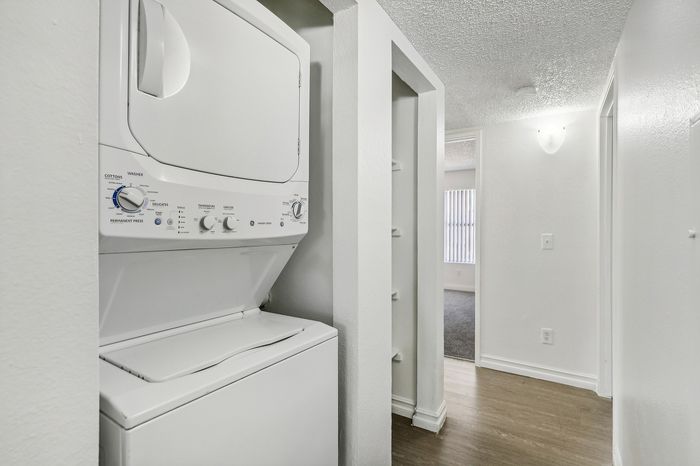 Bright hallway featuring a modern in-unit washer and dryer, leading to a sunlit room with sleek hardwood flooring.