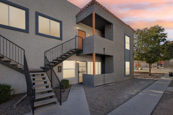 Charming apartment exterior with modern gray facade, stylish balcony, and inviting staircase, set against a picturesque sunset sky.