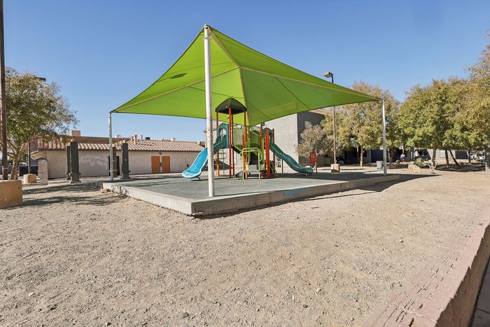 Inviting playground with vibrant slides under a green canopy, surrounded by charming community buildings and lush trees.