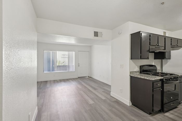 Modern apartment interior with sleek laminate flooring, bright open space, and elegant dark kitchen cabinets.