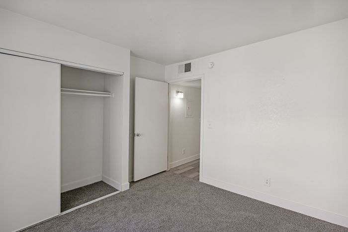 Bright bedroom with plush carpeting, sleek sliding closet doors, and modern white walls.