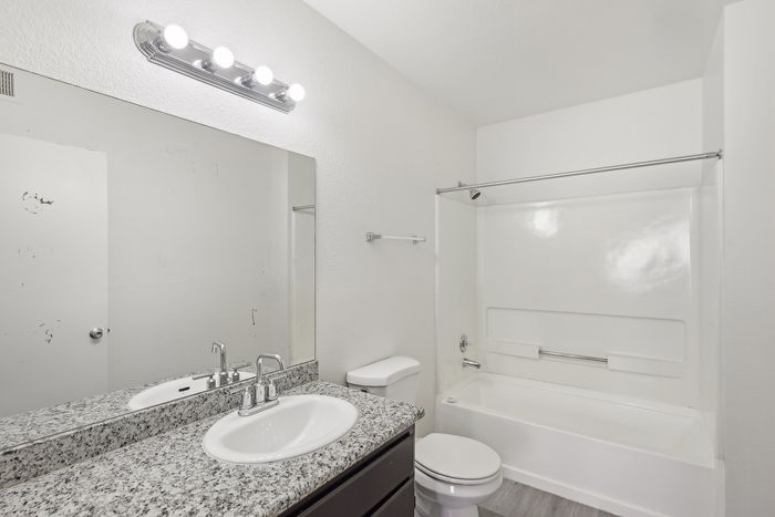 Modern bathroom featuring a sleek granite countertop, large mirror, and a pristine bathtub with contemporary fixtures.