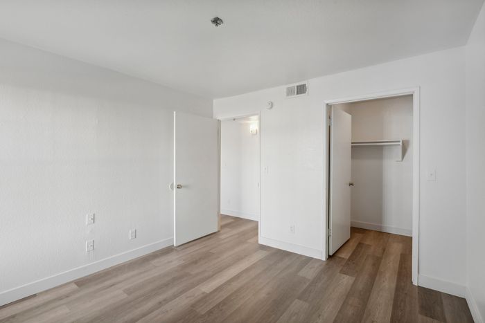 Inviting vacant room with elegant wooden flooring, bright white walls, and a spacious walk-in closet.