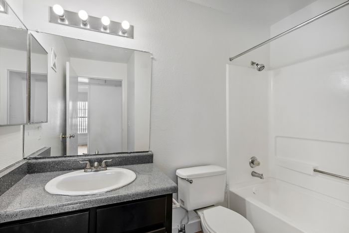 Modern bathroom with sleek design featuring a granite countertop, elegant mirror lighting, and pristine bathtub and sink.