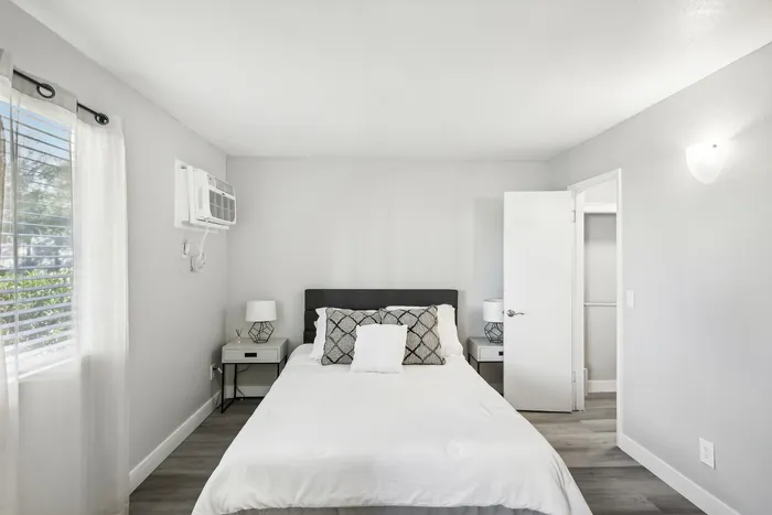 Bright and airy bedroom with modern decor, featuring a cozy bed, sleek nightstands, and a view of lush greenery through large windows.