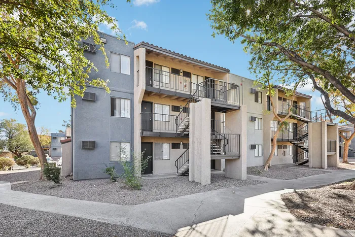 Charming three-story apartment building with outdoor stairs, nestled among trees and landscaped surroundings.