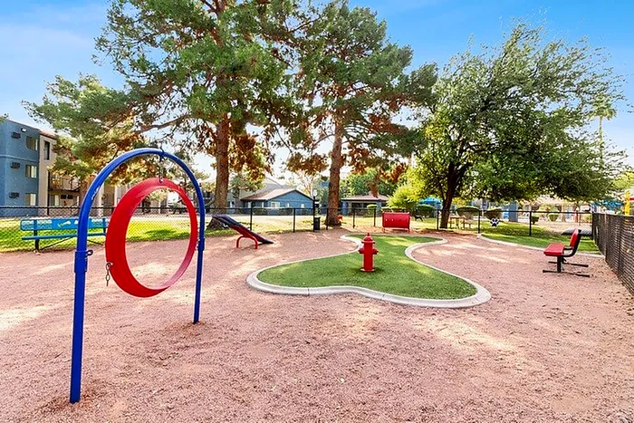 Charming outdoor playground featuring vibrant red and blue play equipment, surrounded by lush greenery and well-maintained communal spaces.