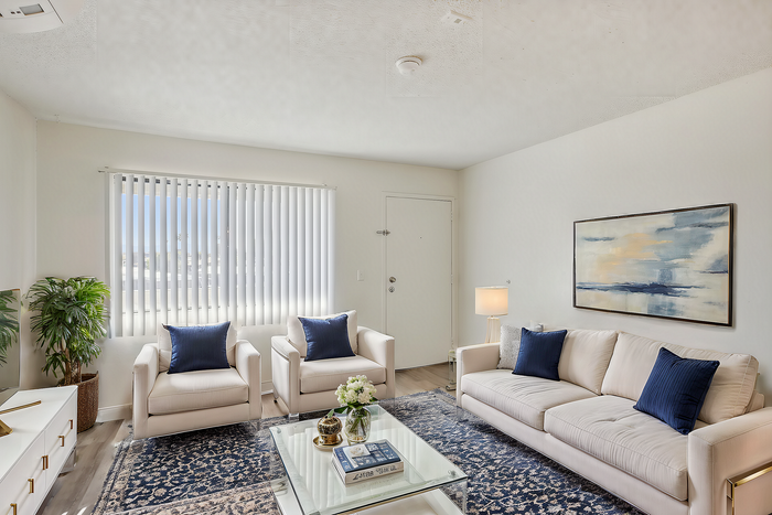 Bright and stylish living room with elegant white sofas, blue cushions, a lush plant, and a modern glass coffee table, exuding warmth and sophistication.