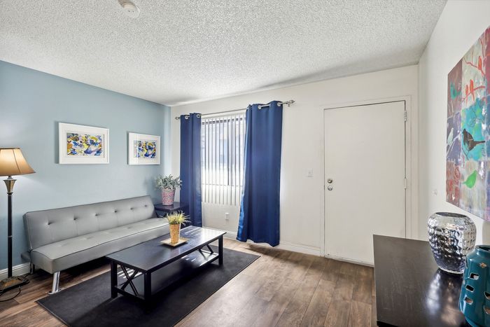 Bright and modern living room featuring a sleek gray sofa, elegant blue curtains, and vibrant artwork, providing a welcoming atmosphere.