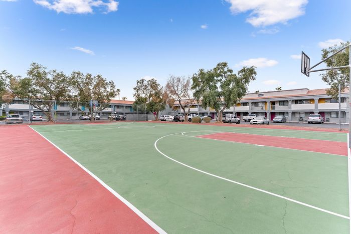 Vibrant apartment complex with a spacious basketball court surrounded by lush trees and ample parking.