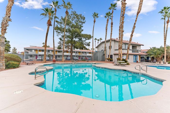 Inviting apartment complex showcasing a sparkling swimming pool, surrounded by palm trees and modern buildings.
