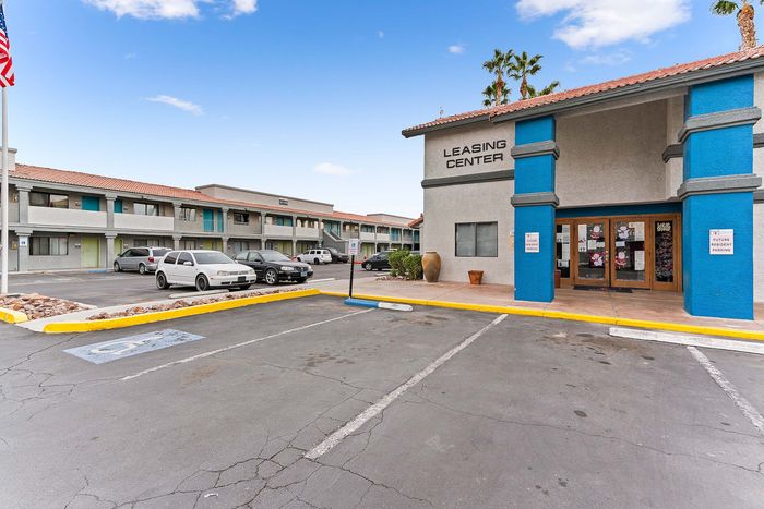 Inviting apartment complex with a vibrant leasing center and ample parking under a clear blue sky.