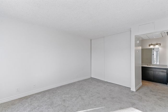 Bright and airy empty room with light gray carpet and sleek closet doors, adjacent to a modern bathroom with elegant lighting.