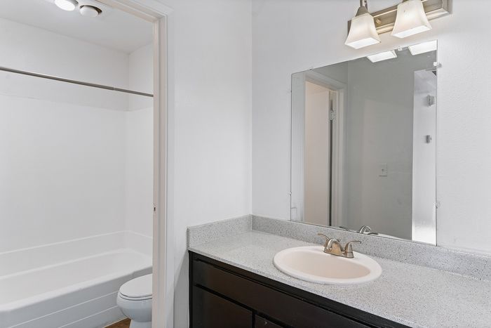 Elegant bathroom with a spacious sink area, updated lighting, and a pristine bathtub, offering a clean and modern ambiance.