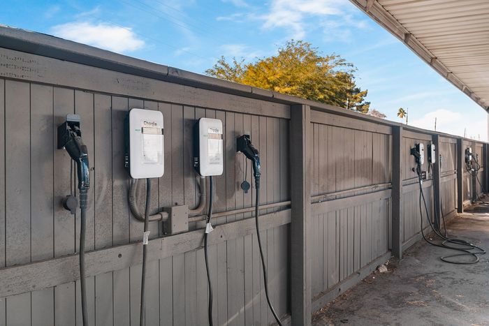 Modern outdoor EV charging station with multiple chargers against a stylish wooden fence, set under a clear blue sky.