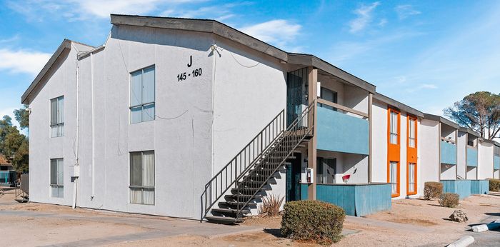 Bright, modern apartment complex with vibrant blue and orange accents, featuring open staircases and sunlit windows, set against a clear blue sky.