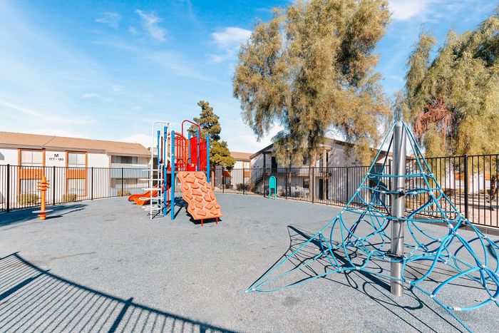 Inviting playground with vibrant climbing structures and slides, surrounded by lush trees and modern apartments, perfect for family-friendly living.