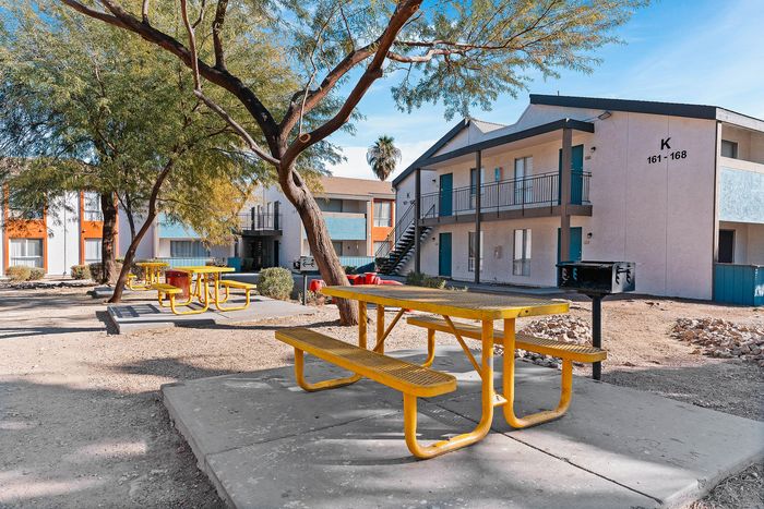 Beautiful apartment complex with vibrant outdoor picnic area, featuring bright yellow tables and lush trees, offering a welcoming community space.