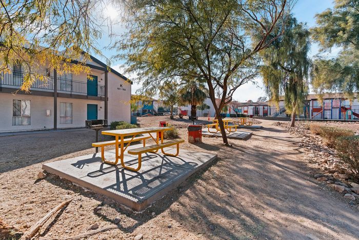 Charming outdoor recreation area with vibrant picnic tables and serene greenery at a welcoming apartment complex under blue skies.
