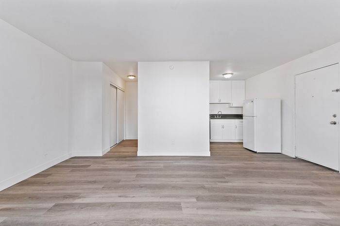 Modern open-plan apartment with sleek wood flooring, a chic white kitchen, and abundant natural light.