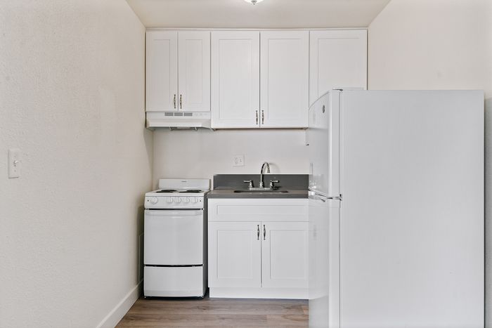 Modern kitchenette with sleek white cabinets, a compact oven, and a spacious refrigerator creating a minimalist charm.