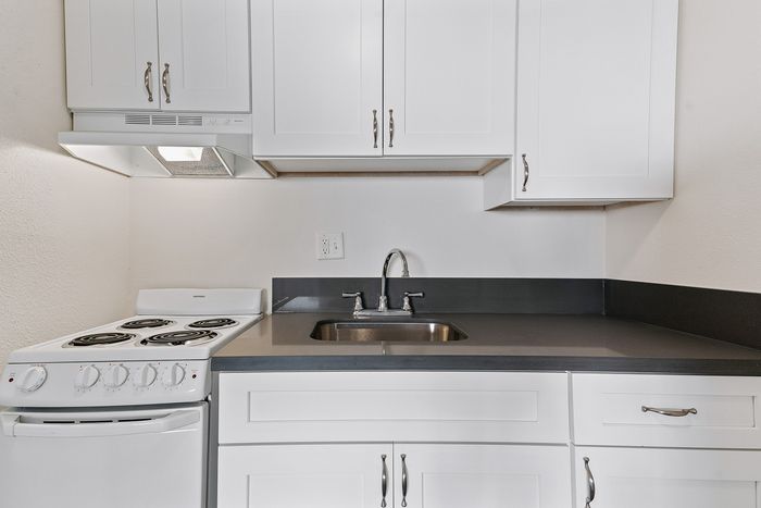 Sleek modern kitchen featuring white cabinetry, stainless steel sink, and electric stove.