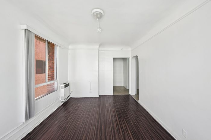 Bright and inviting room with elegant dark wood floors, large window for natural light, and an archway leading to adjoining spaces.