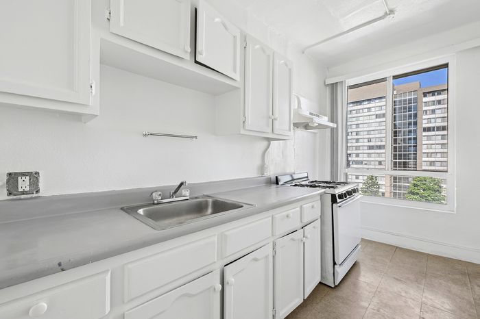 Bright and airy kitchen with modern white cabinets, sleek countertops, and a large window offering a stunning urban view.