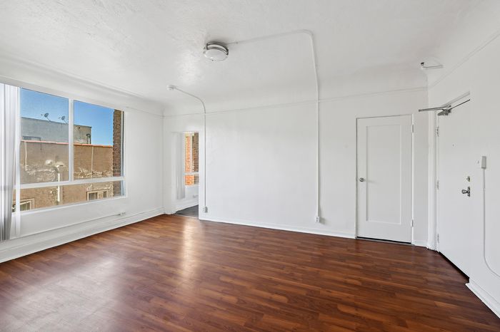 Bright and inviting empty room featuring elegant wood flooring, ample natural light from large windows, and a minimalist white interior.