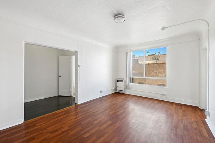 Bright, spacious living room with elegant wood floors, large window with a city view, and modern minimalist design.