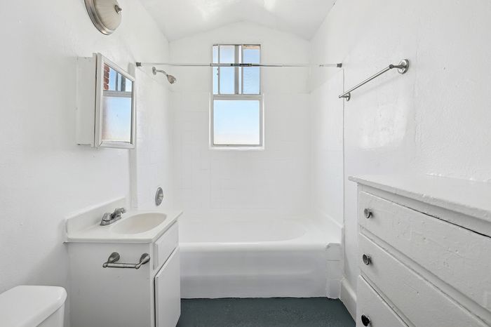 Bright, minimalist bathroom featuring a sleek white tub and vintage fixtures beneath a charming arched ceiling.