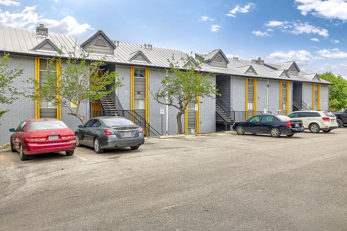 Charming apartment complex featuring modern architecture, ample parking, and vibrant landscaping under a clear blue sky.