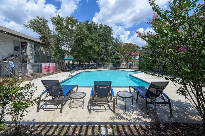 Inviting outdoor pool area with lounge chairs and vibrant greenery, perfect for relaxation and leisure under a bright, blue sky.