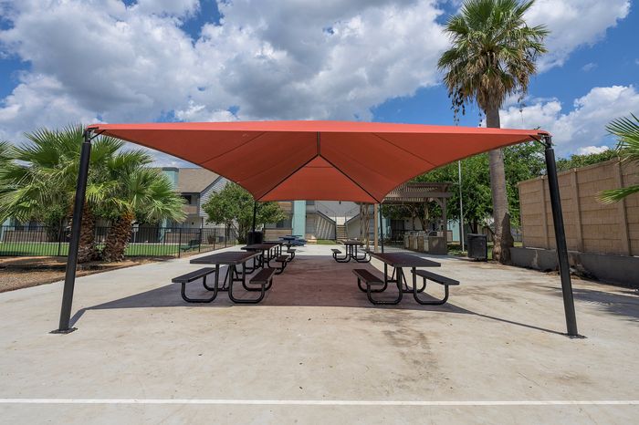 Charming outdoor communal space with shaded picnic tables, surrounded by lush palm trees and clear blue skies.