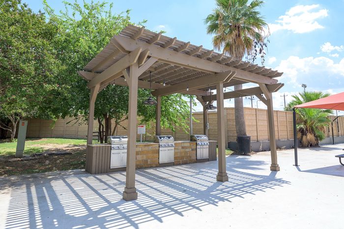 Charming outdoor pavilion with modern grills and lush greenery, perfect for sunny day barbecues.